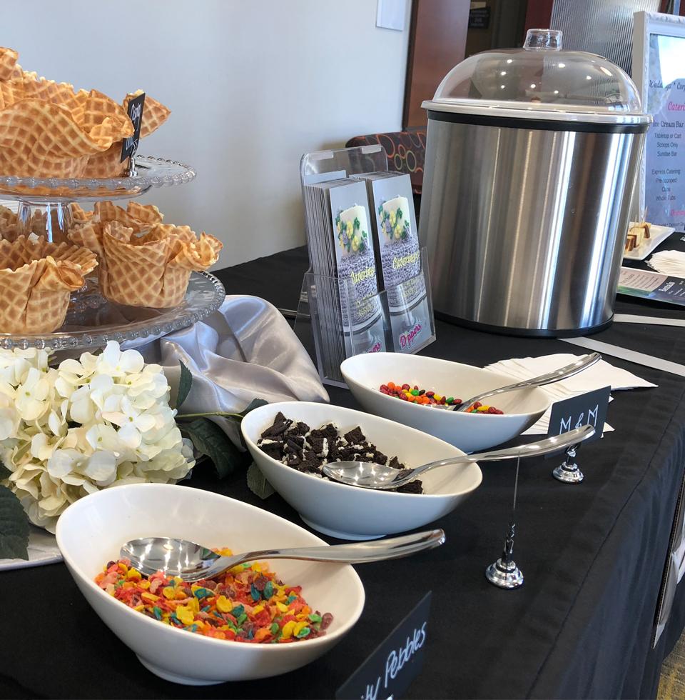 Sundae toppings in bowls alongside an ice cream urn and waffle bowls.